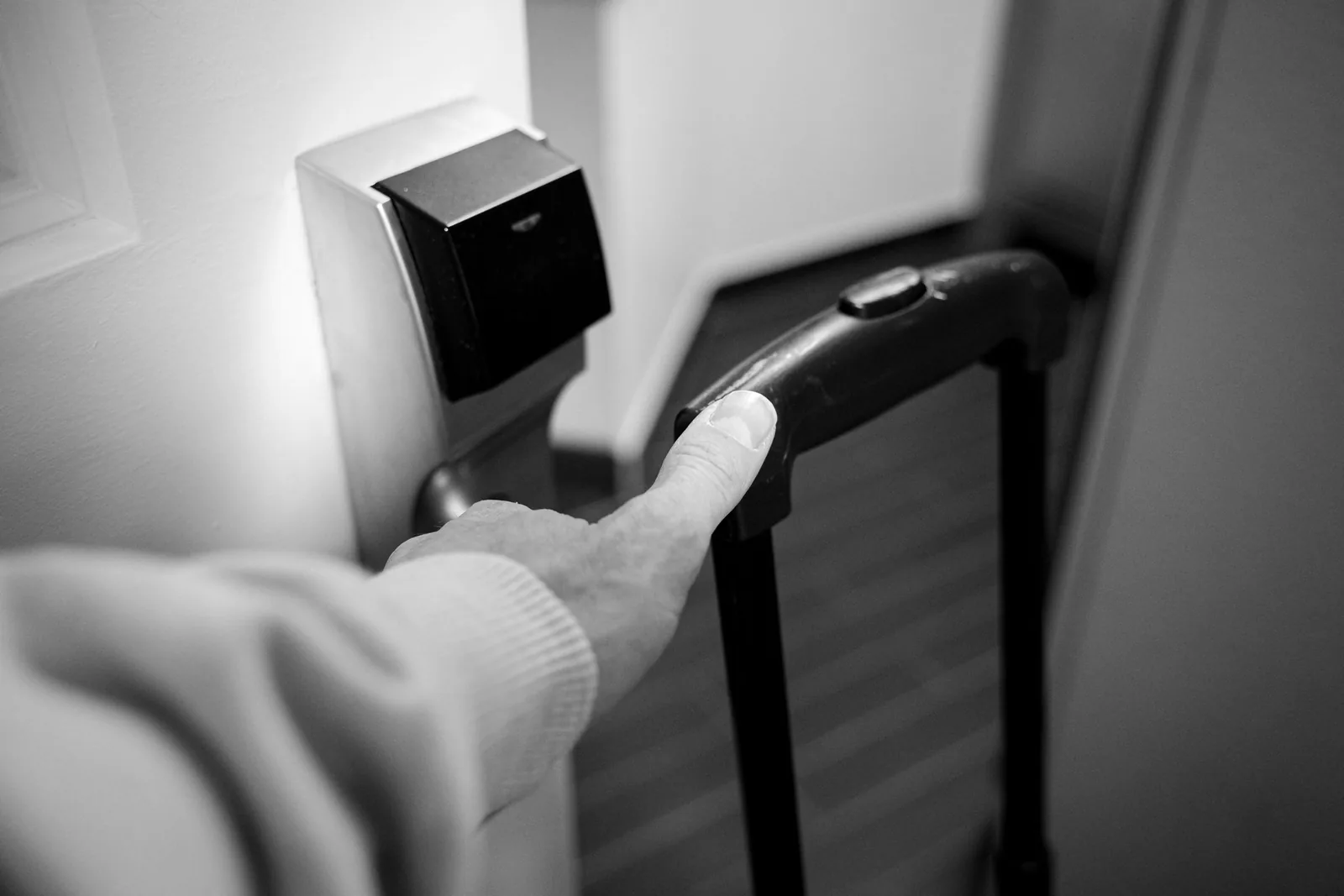 Traveller opening a hotel room door while holding the handle of a suitcase