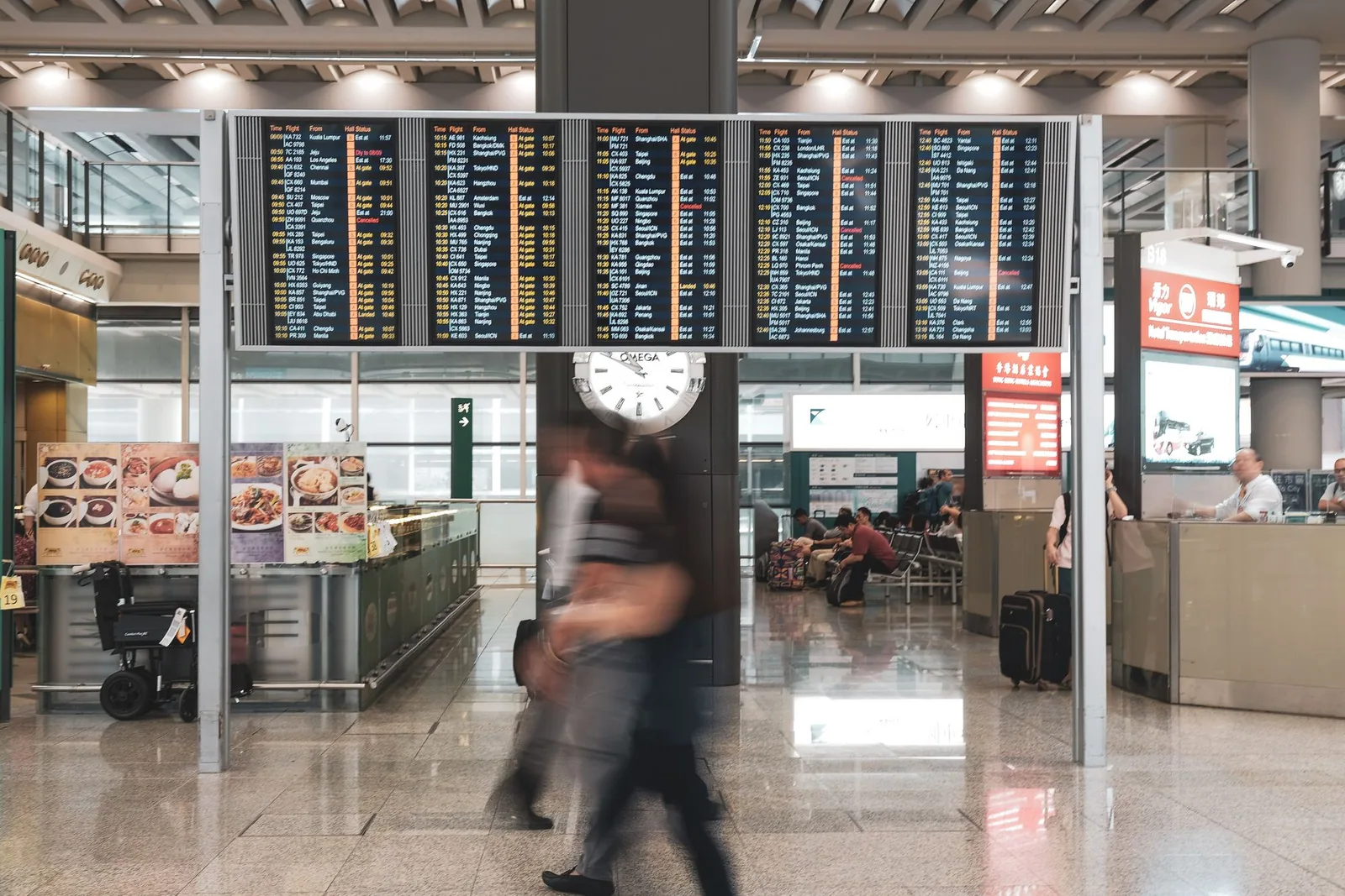 Travellers moving through Hong Kong International Airport beneath departure screens